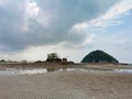 AÃ¢â¬â¹ smallÃ¢â¬â¹ island with mountainÃ¢â¬â¹ and sea rocks onÃ¢â¬â¹ theÃ¢â¬â¹ low tide sandy beachÃ¢â¬â¹ with shallow water and cloudyÃ¢â¬â¹ skyÃ¢â¬â¹